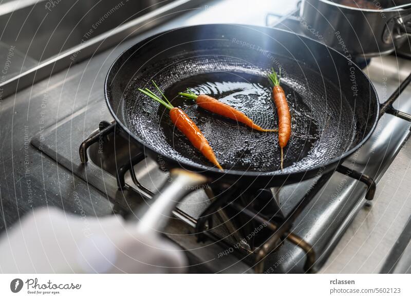 Hand tossing carrots in an oiled pan at a gas stove in a professional kitchen at a restaurant. Luxury hotel cooking concept image. hand vegetables skillet