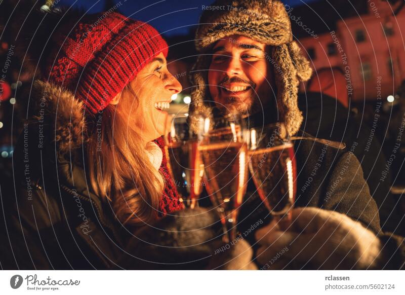 Smiling couple clinking champagne glasses at new years eve group friends christmas market toasting winter evening celebration happy joy outdoor cold