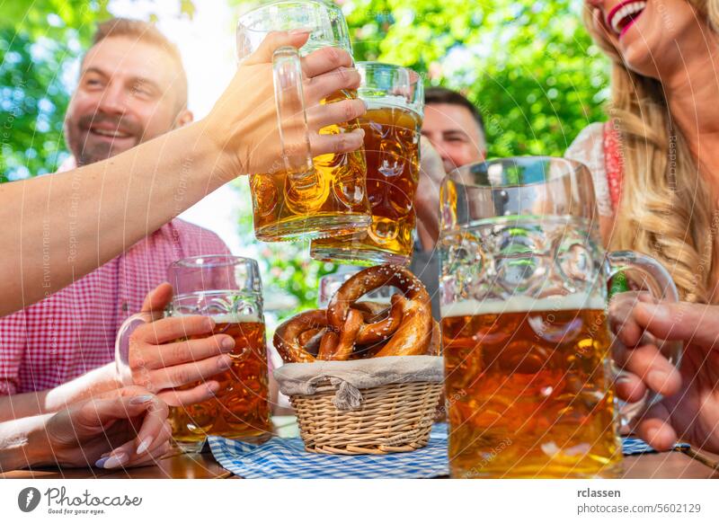 friends in Tracht, Dirndl and Lederhosen having fun sitting on table drinking beer and eating pretzels in Beer garden or oktoberfest in Bavaria, Germany group