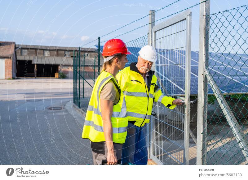 Two engineers in high-visibility vests inspect a solar panel field going in on a facility gate inspection check solar panel facility safety helmets red hard hat