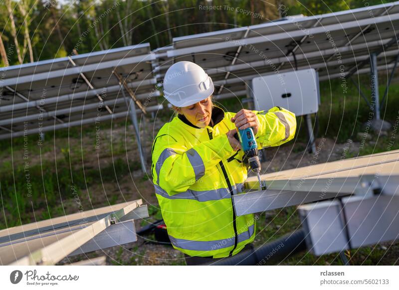 Female technician using a cordless drill on solar panel structure in a field. Alternative energy ecological concept image. technology plant industry electricity