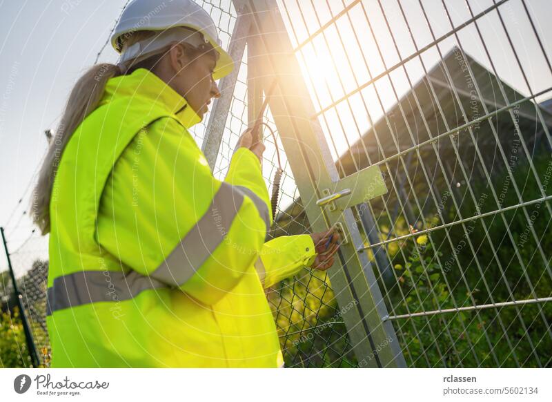 Female technician locking gate at solar panel facility during sunset. Alternative energy ecological concept image. technology plant industry electricity worker
