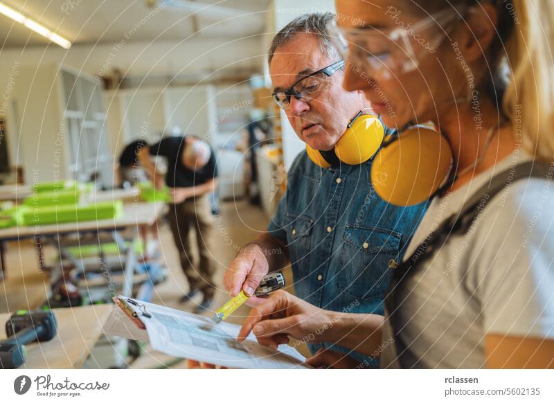 Two carpenters reviewing a blueprint with another working in the background professional craftsman teamwork workbench furniture industry worker carpentry