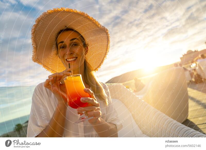 Woman in straw hat sipping a tropical cocktail at tropical beach hotel on sunset with a blurred background paradise beach playa coastline canary island woman