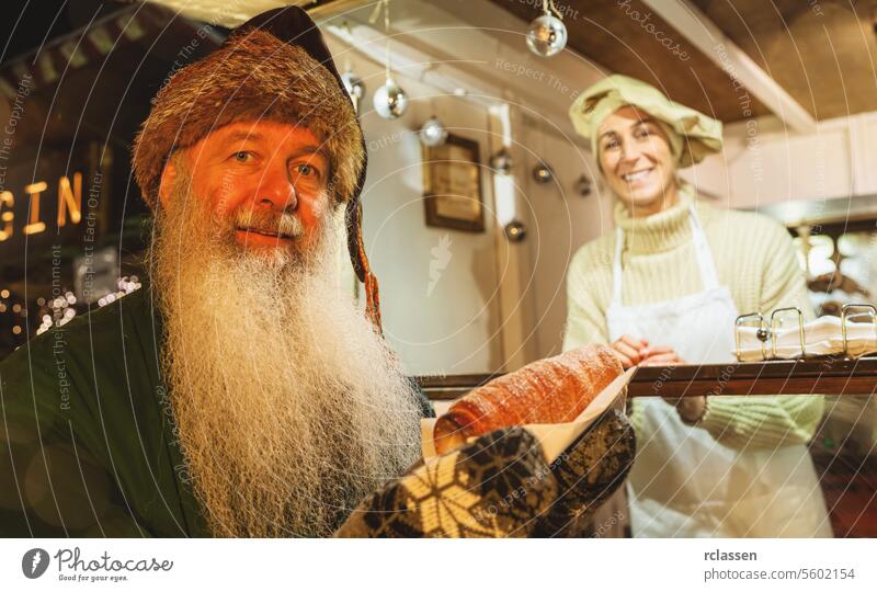 Happy old man holding trdelnik, kurtoscalacs or Baumstriezel in his heand in a Booth at christmas market beard december hungary bread store dessert baumstriezel