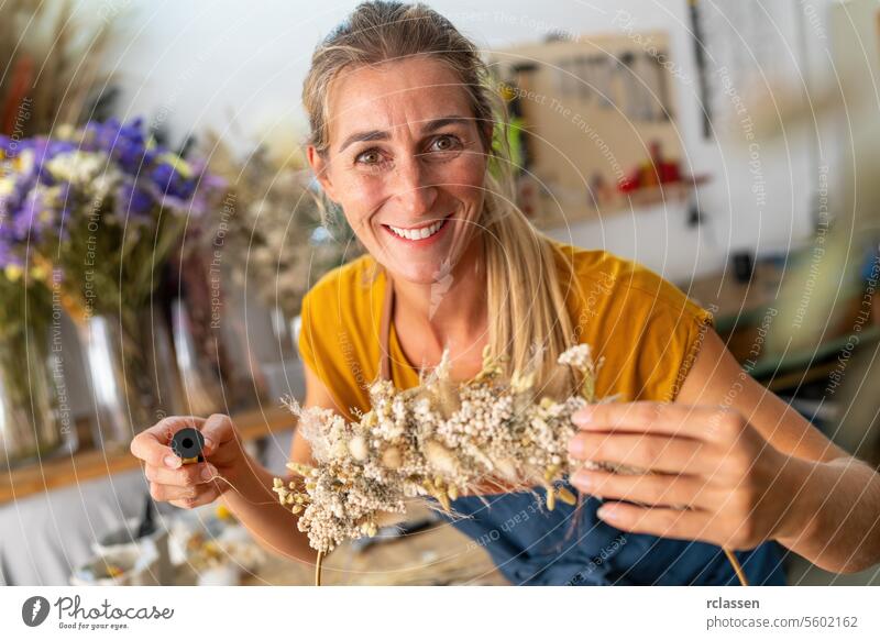 Smiling female florist in a yellow top creating a dried flower arrangement in a workshop wire smiling dried flowers crafting floristry cheerful natural handmade