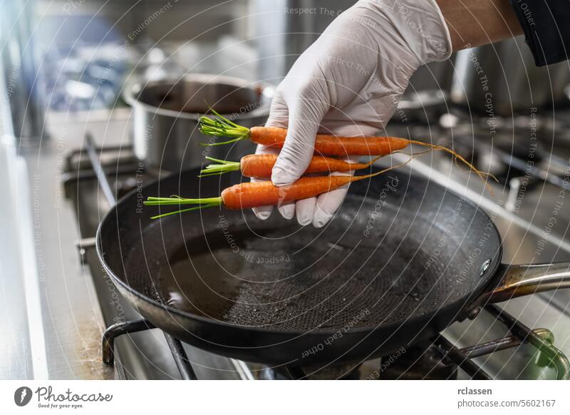 Hand puts fresh carrots into a hot oiled pan at a gas stove in a professional kitchen at a restaurant. Luxury hotel cooking concept image. drop add hand