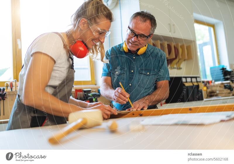 Two carpenters marking measurements on wood in a carpentry workshop hammer professional craftsman workbench furniture industry worker wooden timber earmuffs