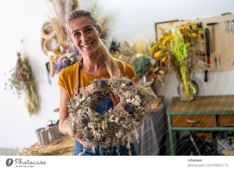 Joyful female florist holding a completed dried flower wreath in a workshop setting joyful floral design handmade natural decoration crafting diy creative