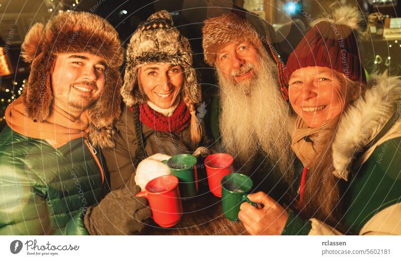 Happy family toasting with mugs of mulled wine and hot chocolate at a Christmas market, wearing winter hats tourist group friends grandparents merry christmas