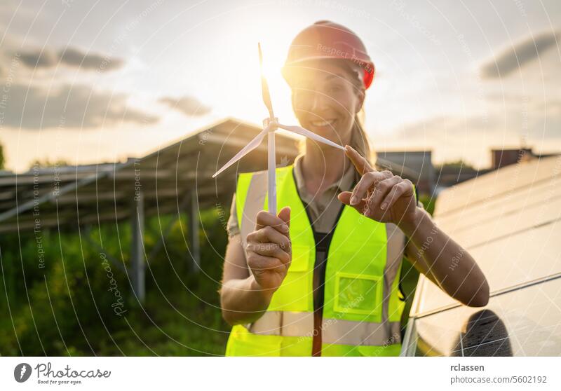 Smiling female engineer holding a wind turbine model at a solar farm. Alternative energy ecological concept image. photovoltaic technology industry electricity