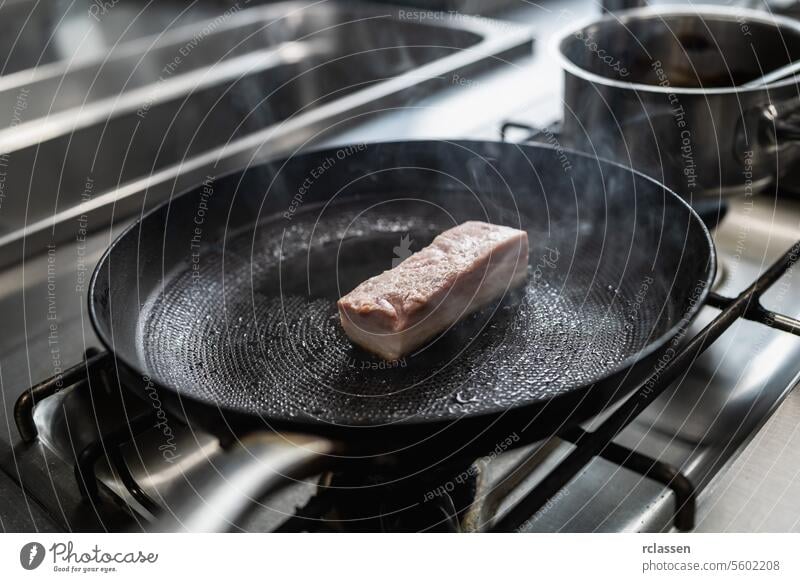 Raw pork Roast in hot pan with oil at a gas stove in a professional kitchen at a restaurant. Luxury hotel cooking concept image. raw crust cuisine steam