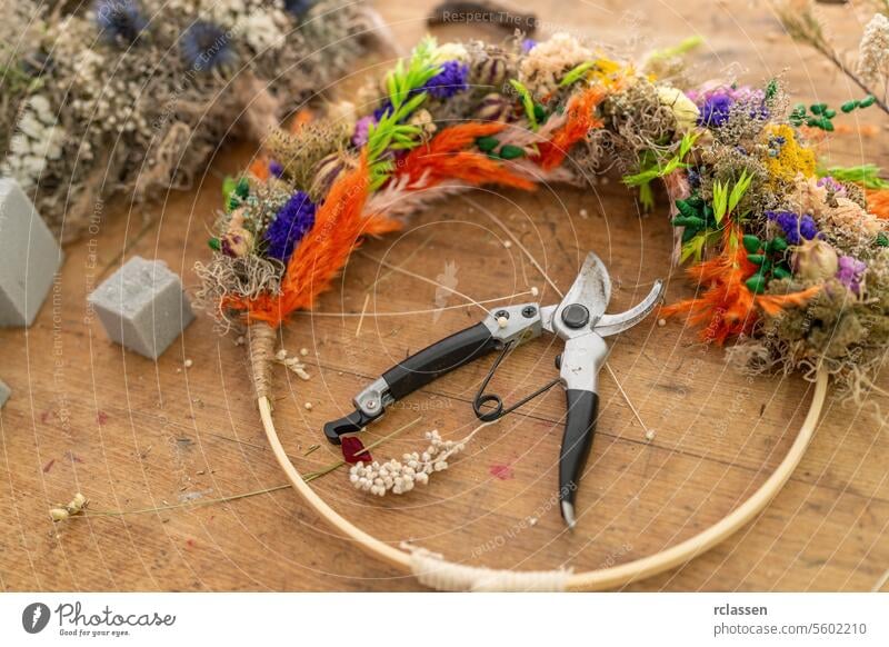 Overhead view of colorful dried flower wreath in progress with florist's scissors on a wooden table overhead view crafting floristry diy botanical handmade