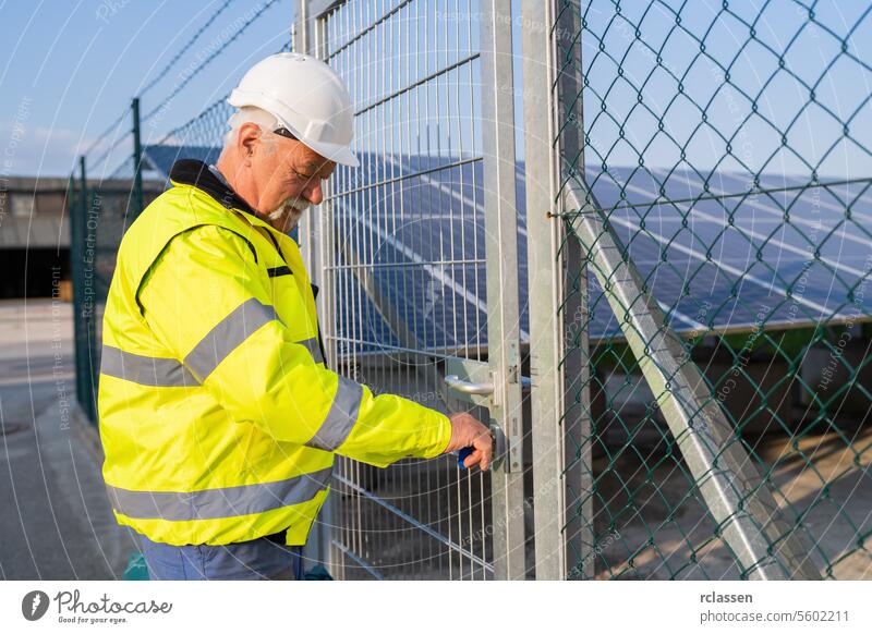 Electrical engineer in safety gear opening a gate to a solar field electrical engineer opening gate reflective vest solar panels chain-link gate