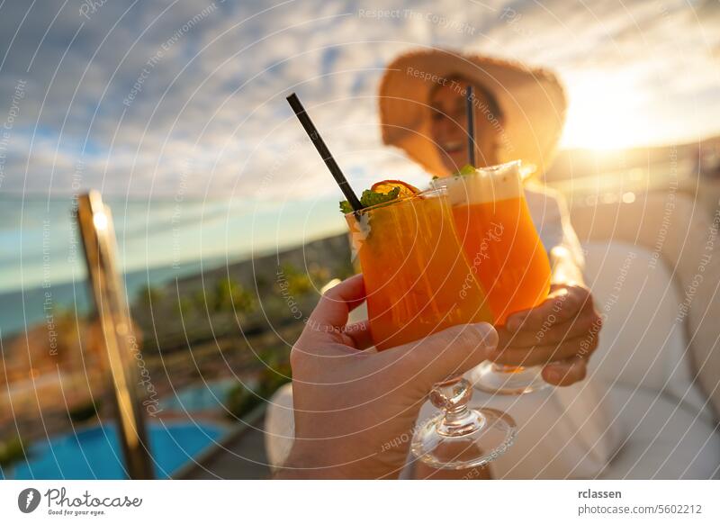 Close-up of a tropical cocktail with a straw held by a woman in a sun hat at tropical beach hotel on sunset paradise beach playa coastline canary island