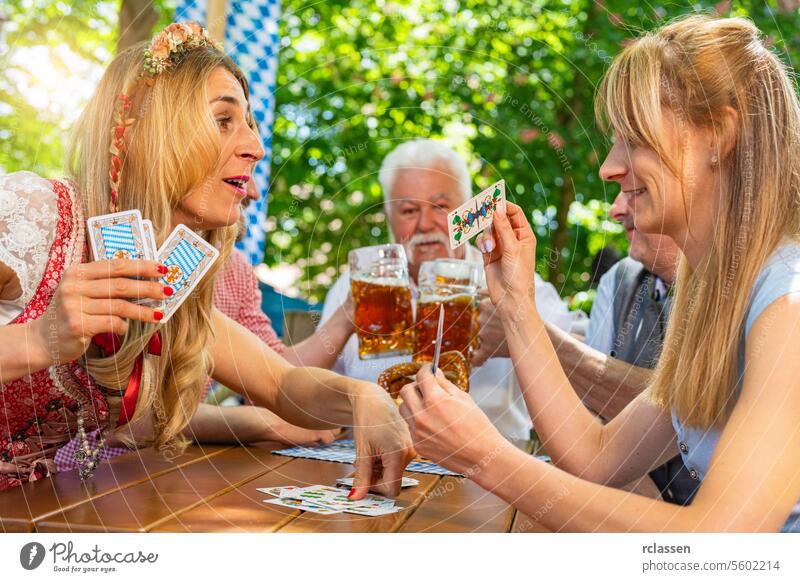 Friends in traditional costume playing traditional card game of Schafkopf in a German beer garden or oktoberfest gambling blockhead cards cheer on pretzels