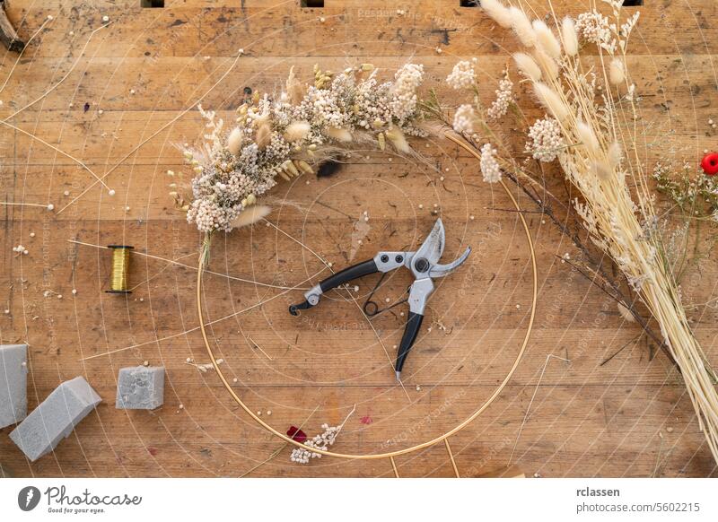 Overhead view of a florist's workspace with the beginnings of a wreath, tools, and materials overhead view wreath beginnings floristry diy wooden table