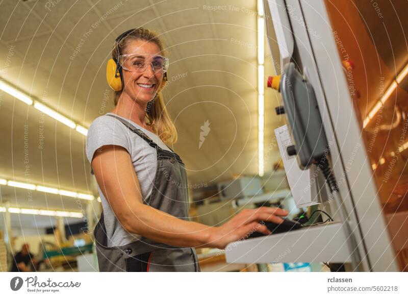 Woman using a computer on a cutting machine in a carpentry workshop experienced craftsman earmuffs safety glasses professional craftsman workbench