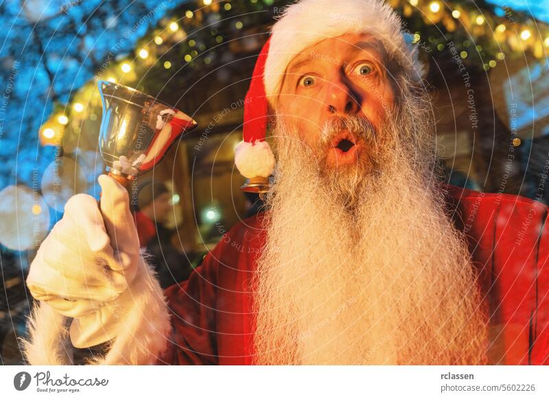 Santa Claus with surprised look, ringing a bell at a Christmas market, festive lights backdrop tourist joyful merry christmas gloves traditional mulled wine