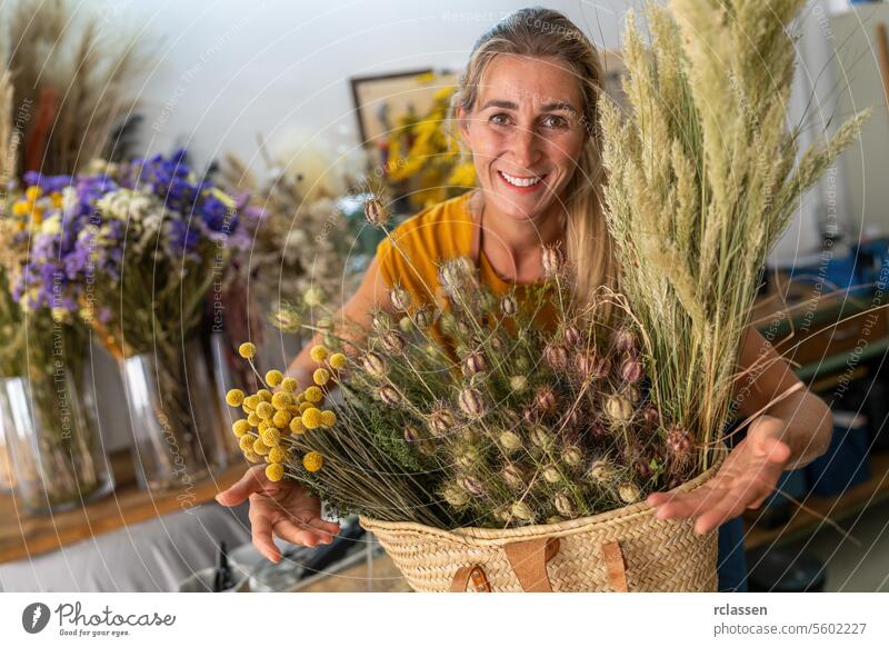 Happy florist holding a basket of dried flowers in a floral shop happy woman smiling natural decoration artisan botanical workshop crafting bouquet floristry