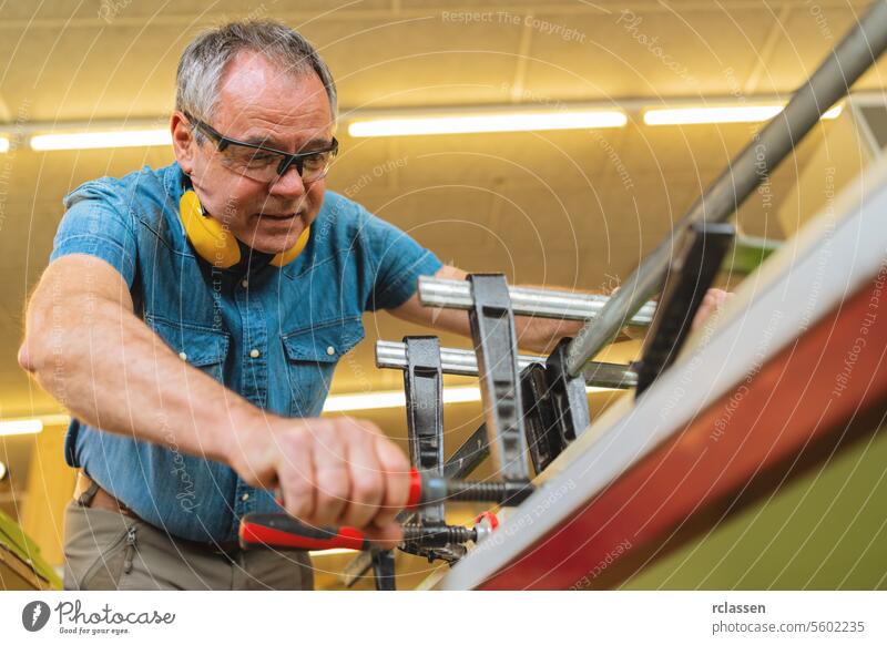 Focused Carpenter with hearing protection working with clamps and wood in a workshop professional craftsman workbench furniture industry worker wooden timber