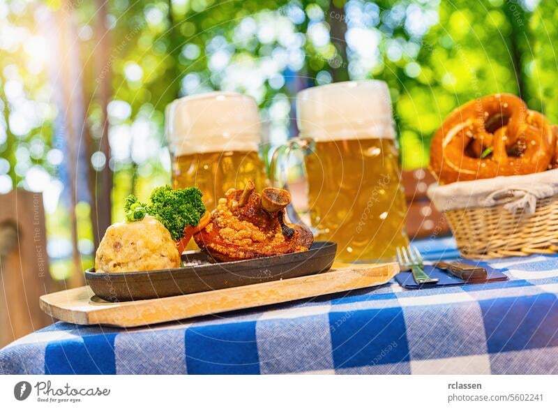 Schweinshaxe, traditional Bavarian cuisine with roasted ham hock (pork knuckle) with potato dumpling, brezen and beer mug on a table at beer garden pretzels
