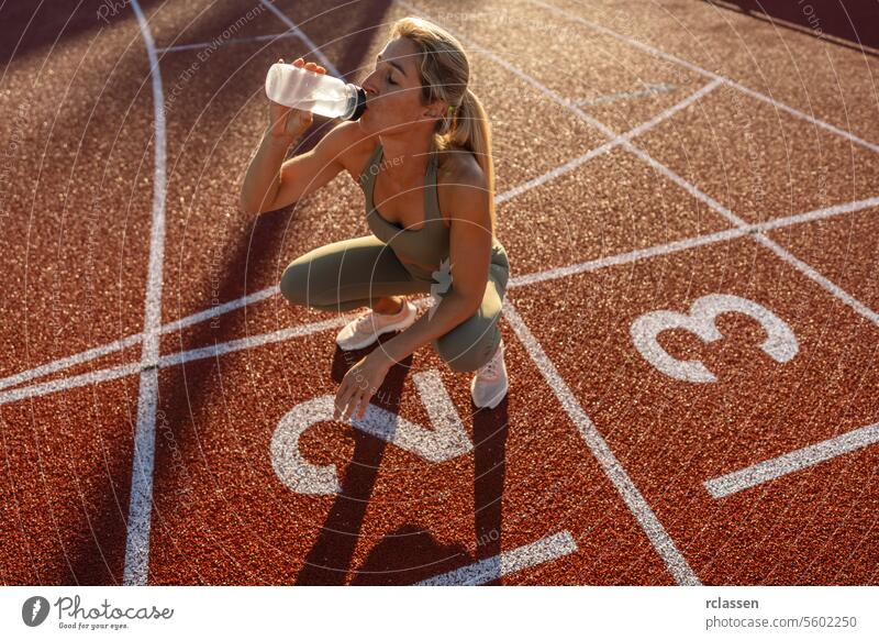 Athlete woman drinking water while crouching on a track field at sunset athlete hydration fitness sportswear health wellness exercise outdoor training