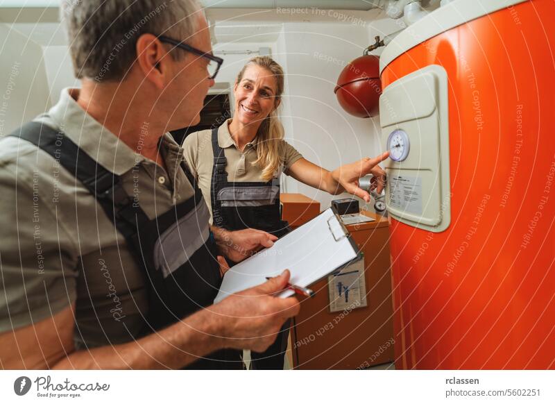 Team of heating engineers checks a old gas heating system thermostat, holding a Clipboard with checklist at a boiler room in a house. Gas heater replacement obligation concept image