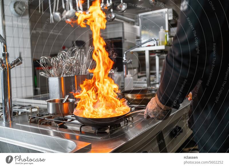 Pro chef flambeing in the kitchen in a pan on a gas-fired stove. Luxury hotel chef cooking concept image. flame culinary professional kitchen stainless steel