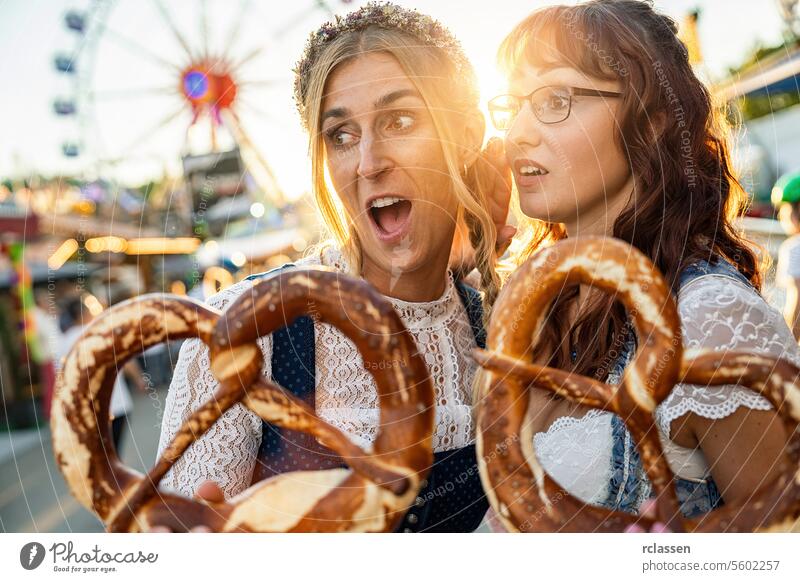 Two girlfriends look amazed with pretzel or brezen on a Bavarian fair or oktoberfest or duld in national costume or Dirndl woman party beergarden dirndl