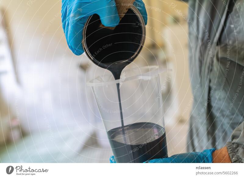 Close-up of hands pouring black paint into a clear measuring cup with blue gloves carpenter craftsman mask spray gun painter pouring paint close-up