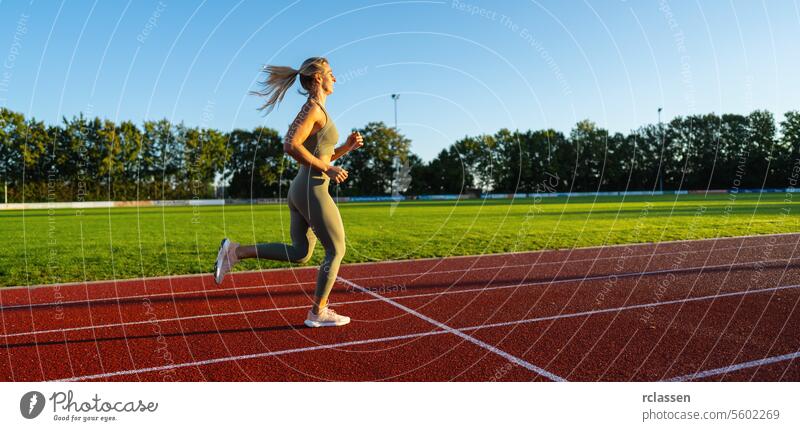 Female athlete running on a sunny track field summer stadium grass field motion female runner track and field athletics jogging fitness sportswear