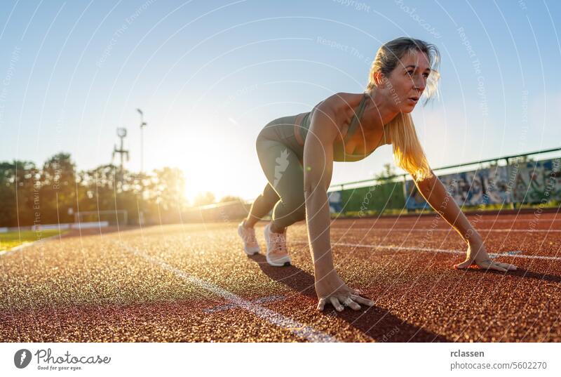 Female athlete in starting position on a track field during sunset female athlete determination sportswear fitness sprinter active lifestyle competition racer