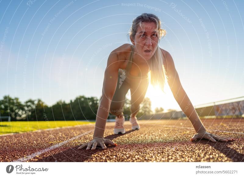 Intense female athlete at starting line on race track during sunset intense determination sportswear fitness ready to run sprinter competitive track and field