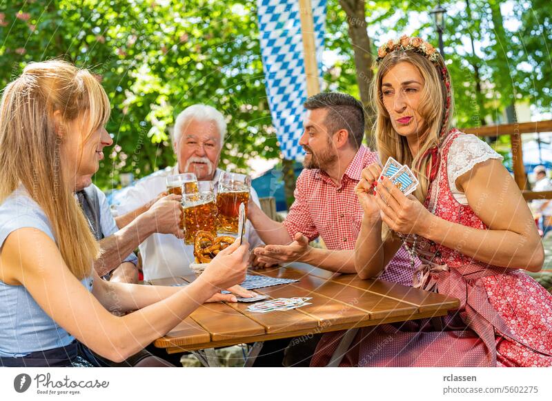Bavarian people in traditional costume playing traditional card game of Schafkopf in a German beer garden or oktoberfest gambling blockhead cards cheer on