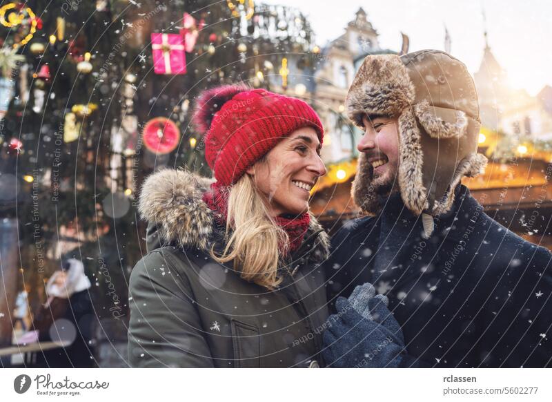 Couple in love smiling affectionately at each other in a snowy Christmas market friends mulled wine boyfriend beard tourism dating fair travel happy couple