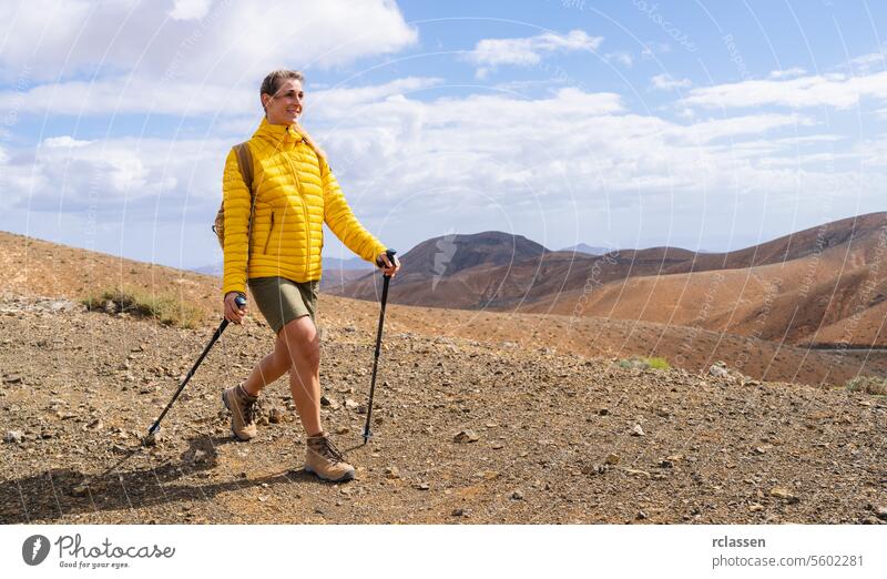 Smiling hiker in yellow jacket with trekking poles in mountainous desert terrain fuerteventura mountains smiling outdoor adventure hiking trail nature
