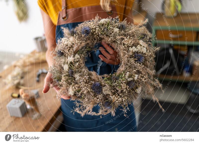 Florist presenting a nearly finished dried flower wreath, showcasing its textures and colors florist workshop handmade botanical crafting diy creative natural
