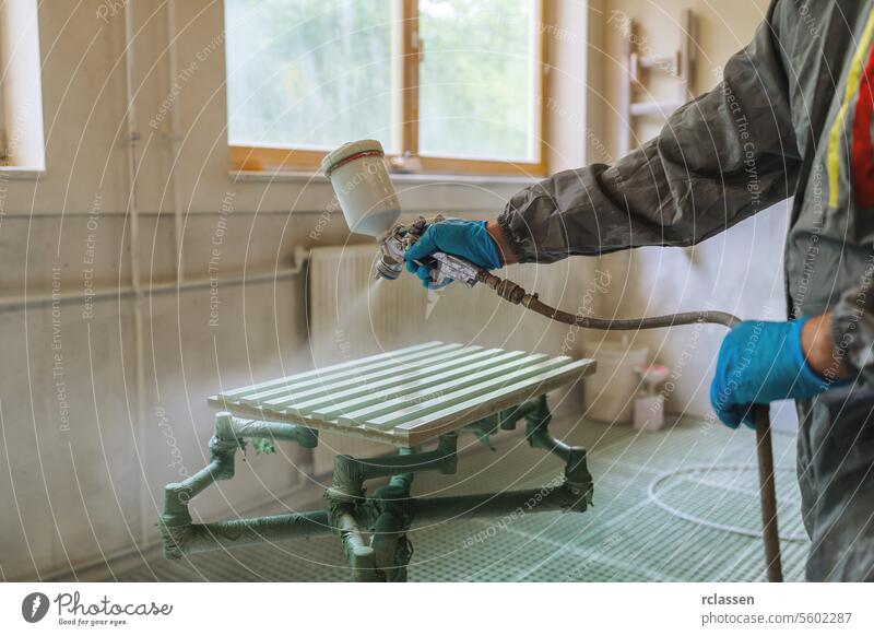 Person in a protective suit spray painting a wooden panel in a carpentry workshop carpenter craftsman mask spray gun painter protective gear gloves