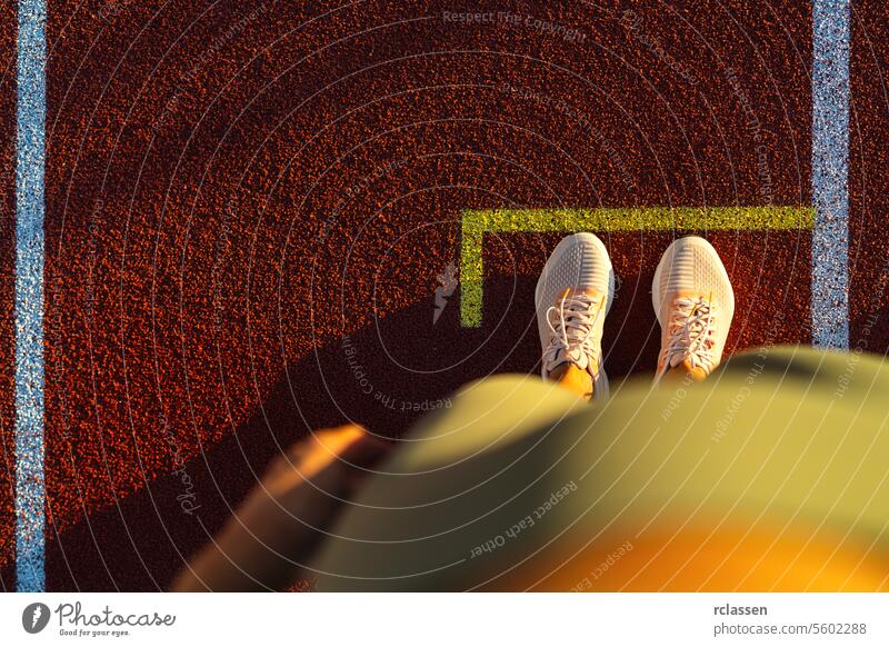 Top-down view of a person's feet at the start line on a running track athletic shoes sports competition track and field runner's view top-down perspective