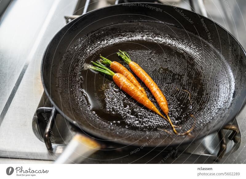 Carrots frying in oiled pan at a gas stove in a professional kitchen at a restaurant. Luxury hotel cooking concept image. vegetables carrots skillet sautéing