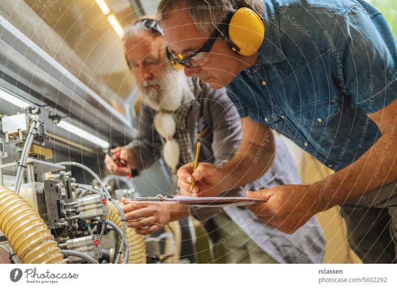 Two men with ear defenders working on machinery in a woodworking shop technicians industrial carpentry adjusting teamwork safety equipment collaboration