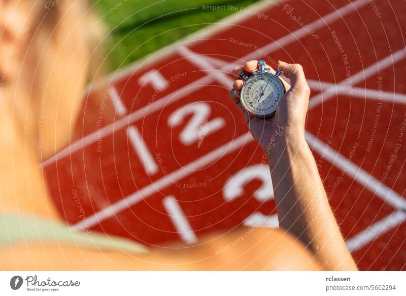 Over-the-shoulder view of a person holding a stopwatch at a running track woman athletics sport hand numbers competition track and field red outdoor timekeeper