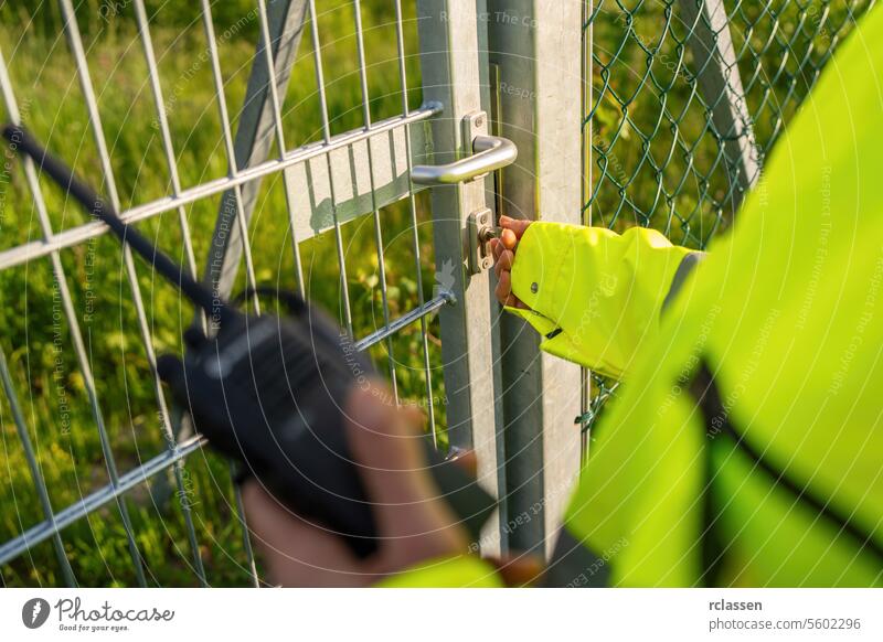 Security personnel unlocking a gate with a walkie-talkie in hand key safety communication metal gate secure access radio entrance locking mechanism
