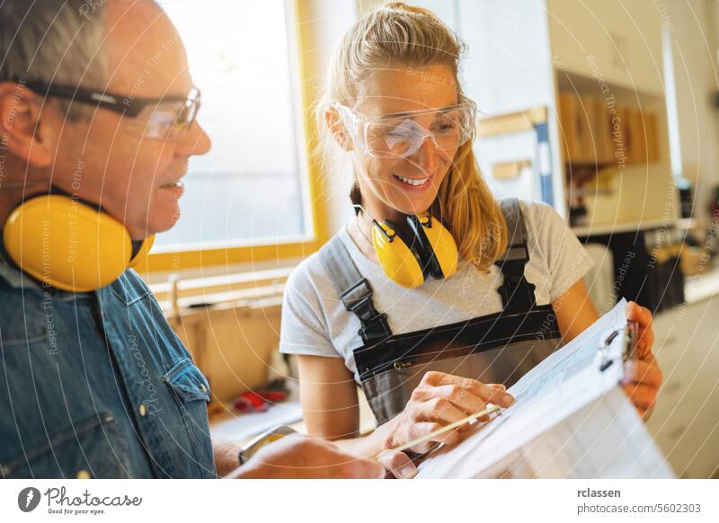 happy carpenters examining a blueprint in a carpentry professional craftsman teamwork workbench furniture industry worker earmuffs safety glasses protection