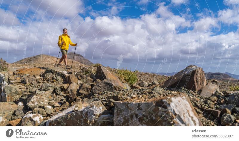 Hiker in yellow on rocky mountain terrain with cloudy blue sky in the background fuerteventura hiker yellow jacket clouds outdoor adventure hiking trekking