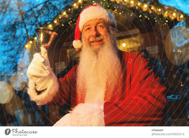 Santa Claus holding a bell with a joyful expression at a Christmas market with festive lights santa claus holding bell christmas market holiday cheer red suit