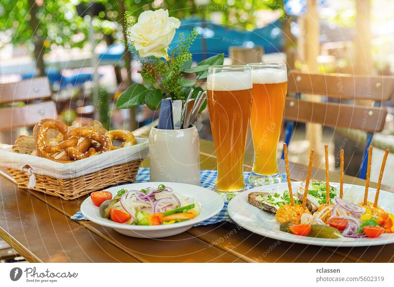 Traditional beer garden food with obatzter beer mugs with fresh pretzels or brezen and bread at Oktoberfest, Munich, Germany cheers waiter wheat beer radish