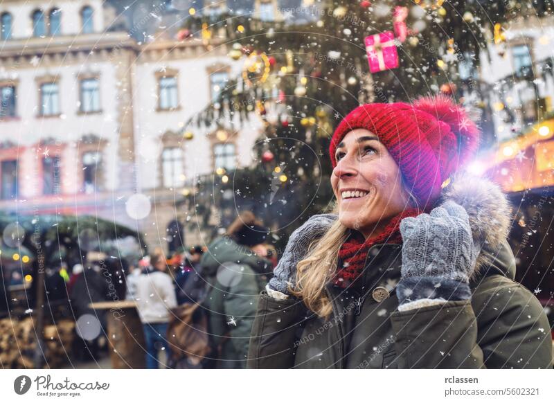 Joyful woman in red beanie looking up at falling snow at a Christmas market, with copyspace for your individual text. merry christmas hot chocolate gloves
