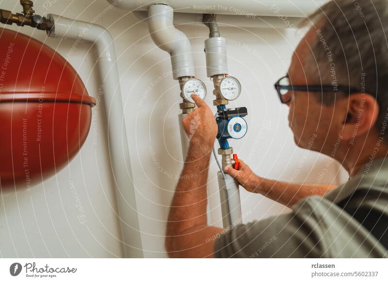 Heating engineer checks gas thermostat at a boiler room with a old gas heating system. Gas heater replacement obligation concept image glasses man read